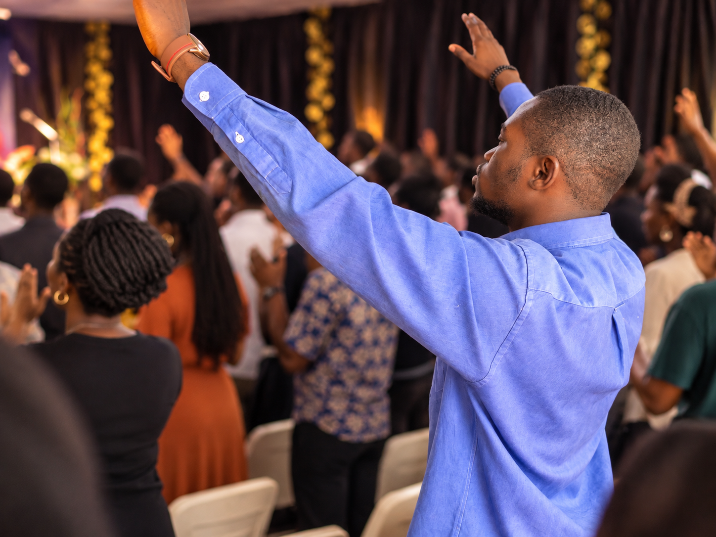 Worshipper in a blue shirt raising his hands during a church service